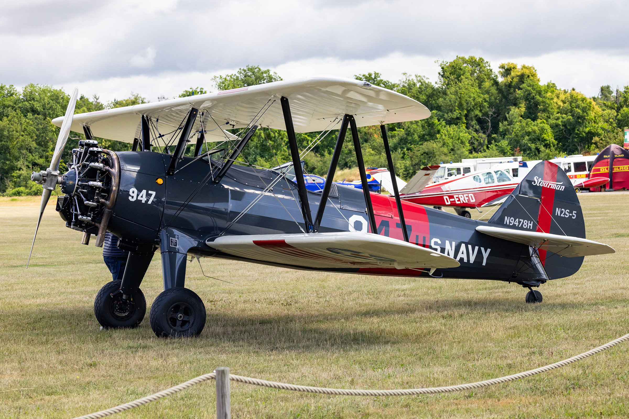 The gallery image of the static display of the dark and white-painted Boeing B75N1 Stearman “N9478H” at the Bienenfarm in Brandenburg as part of the “Stearman & Friends 2026” event.